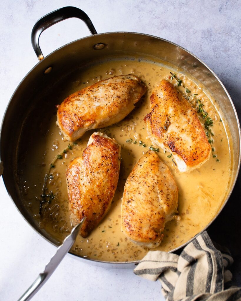 Pan Seared chicken breasts in sherry cream pan sauce in a sauce pan with a serving spoon.