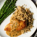 Pan Seared Chicken breast with sherry cream pan sauce, rice and asparagus on a white plate.