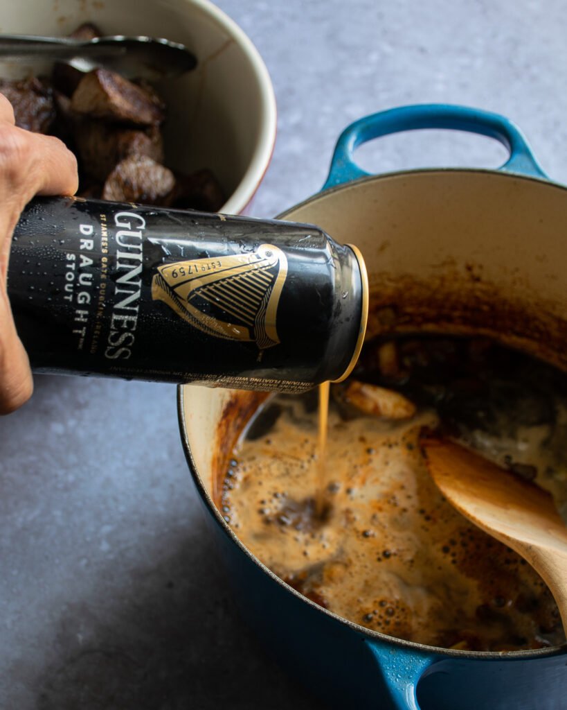 A can of Guinness stout being poured into a pot of beef stew.