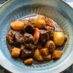 Guinness Stew in a blue bowl on a blue and white checkered placemat.
