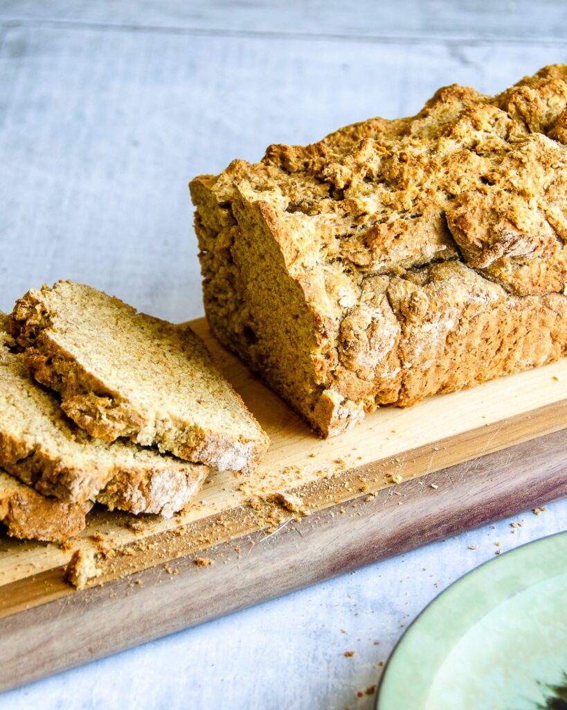 Irish Brown Soda Bread on a cutting board with a few slices already sliced out of it.