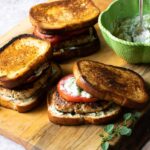 Greek Turkey Burgers on a cutting board with a green bowl of Tzaziki sauce.