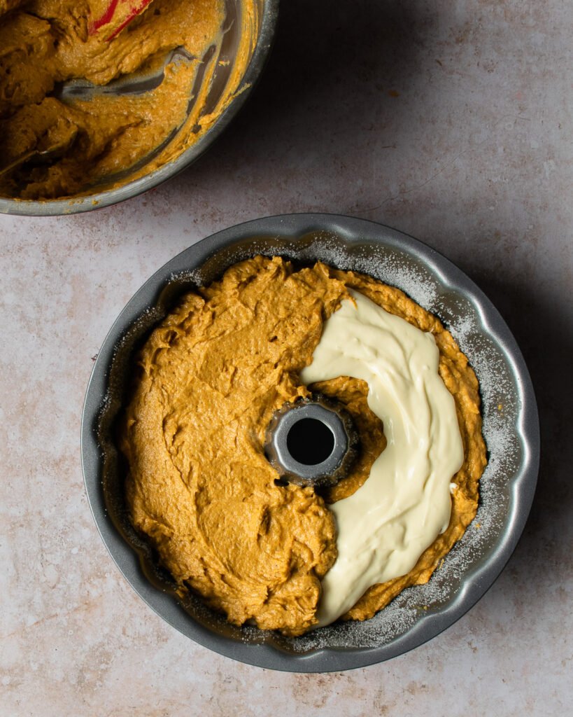 Batter going on top of cream cheese filling in a Bundt pan.
