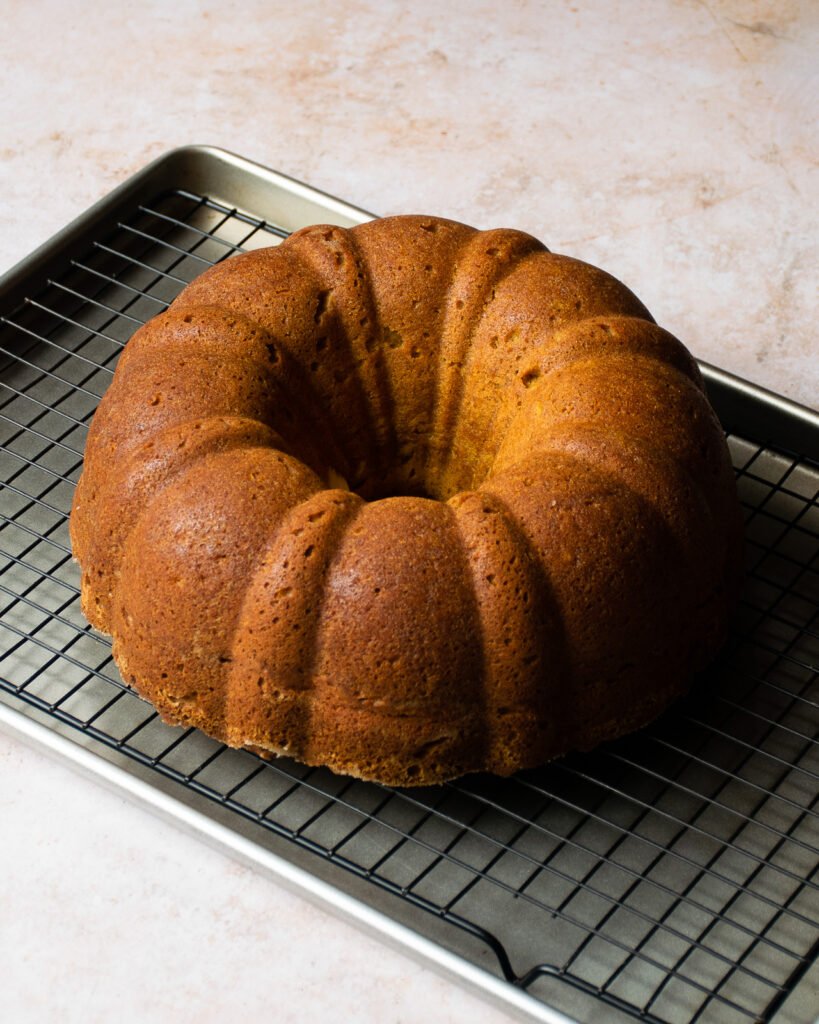 Pumpkin bundt cake unfolded and sitting on a rack over a sheet pan, ready to be glazed.