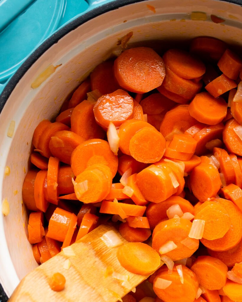 Carrots cooking in a Dutch oven with a wooden spoon sticking out of them.