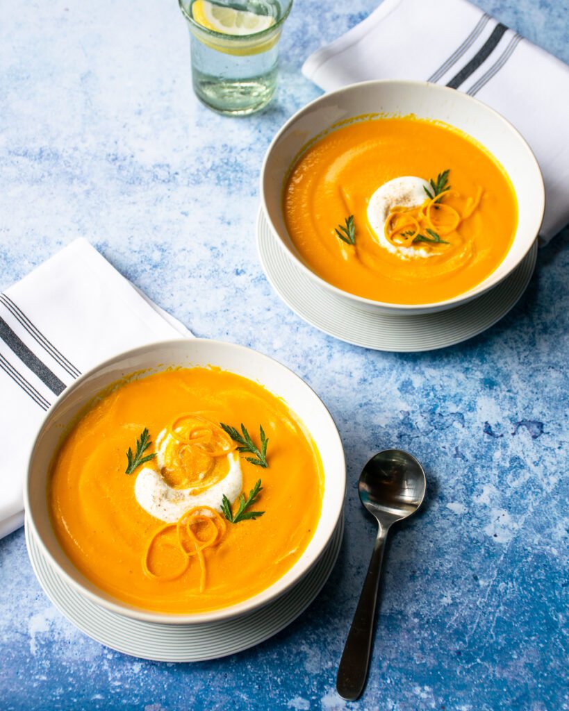Two bowls of carrot ginger orange soup, garnished with shipped cream.