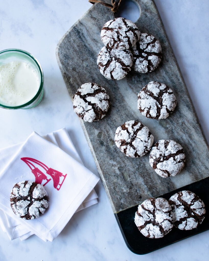 Chocolate Crinkle Cookies on a marble tray with napkins and a glass of milk.