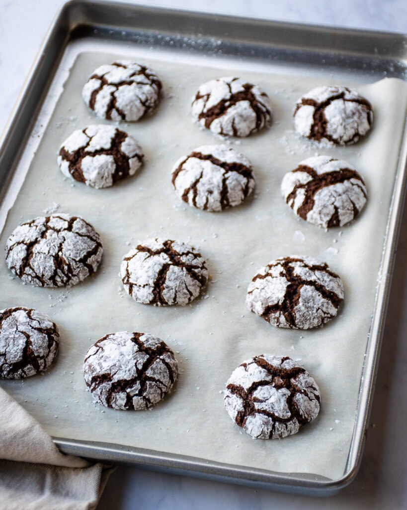 Chocolate Crinkle Cookies fully baked on a parchment lined baking sheet.