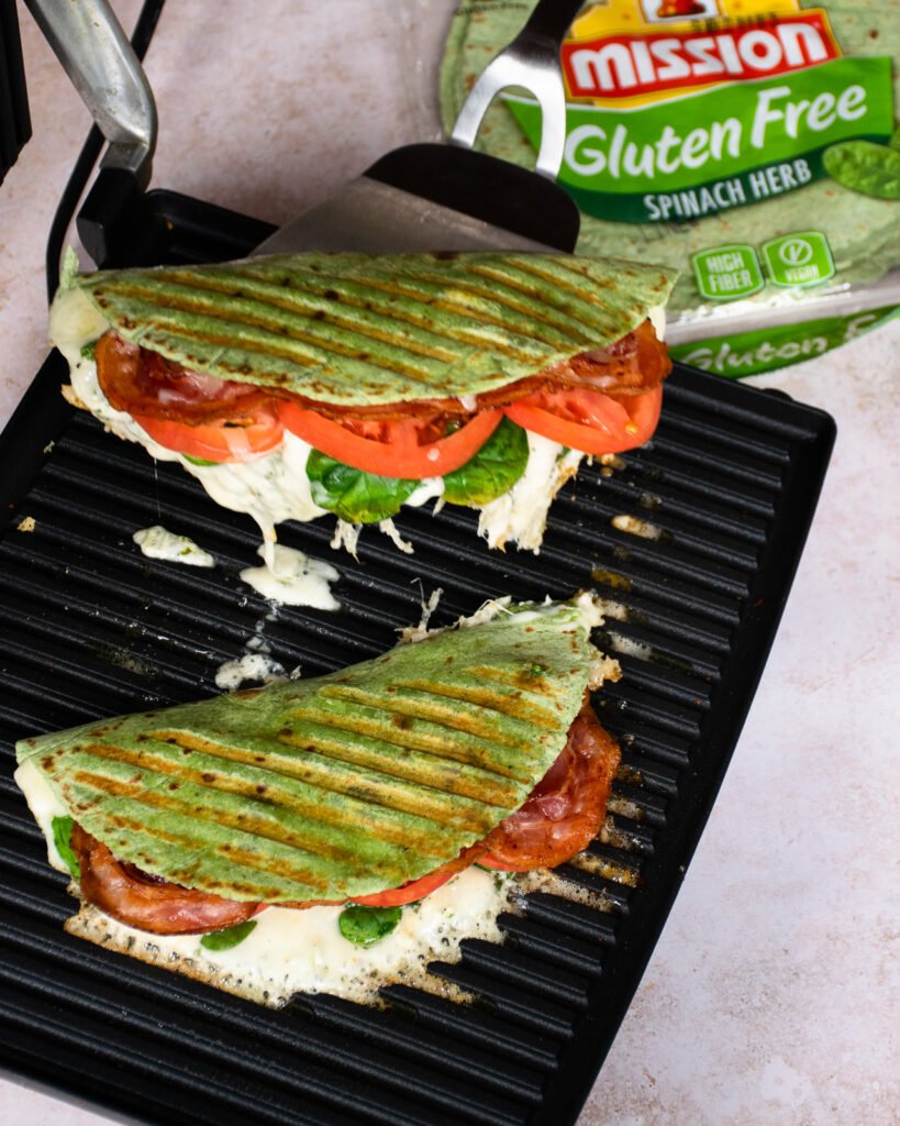Two paninis on a panini maker with a package of tortillas near by.