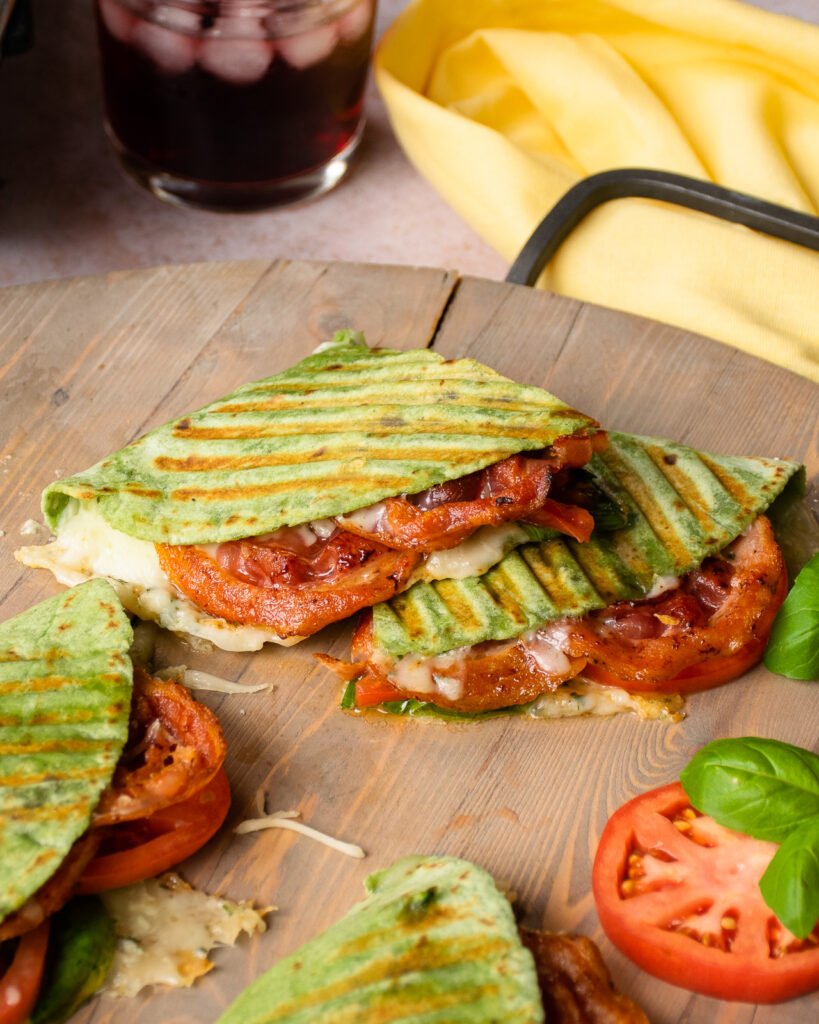 Italian BLT Panini cut on a cutting board with a yellow napkin in the background.