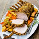 Pork Rib Roast with Root vegetables on a white platter on a wooden table.