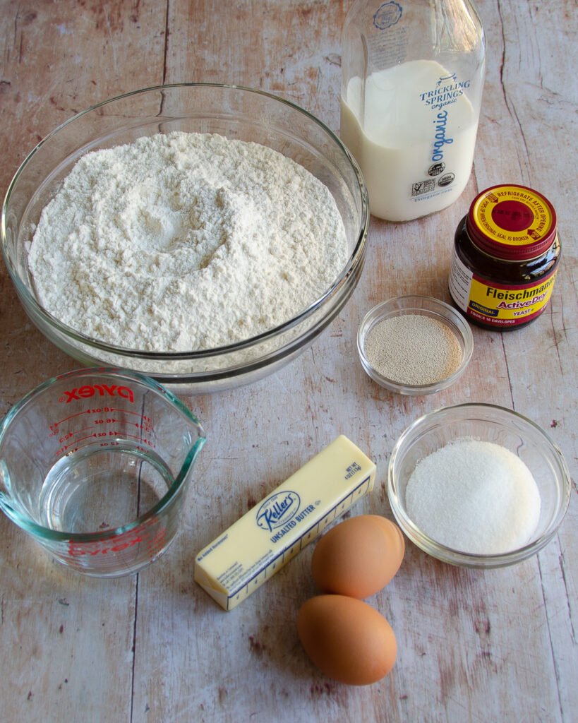 Ingredients on a wooden table - eggs, butter, water, sugar, yeast, milk and flour.