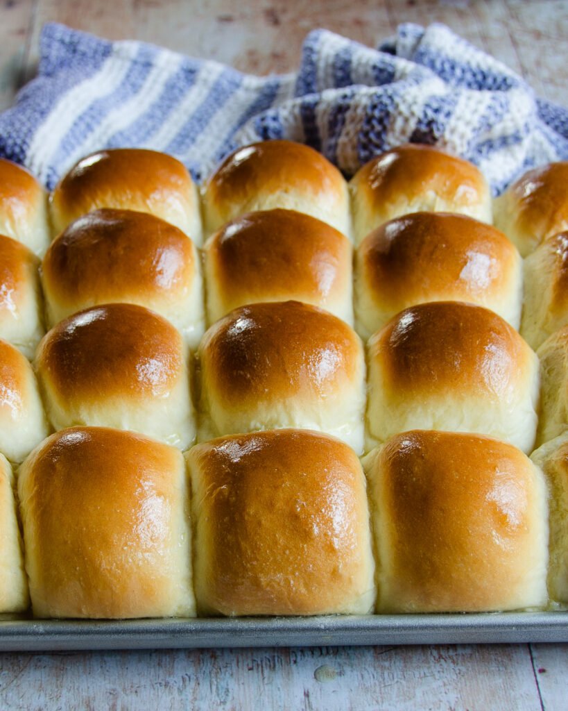 Sheet Pan Dinner Rolls on a sheet pan with aa blue and white striped towel in the background.