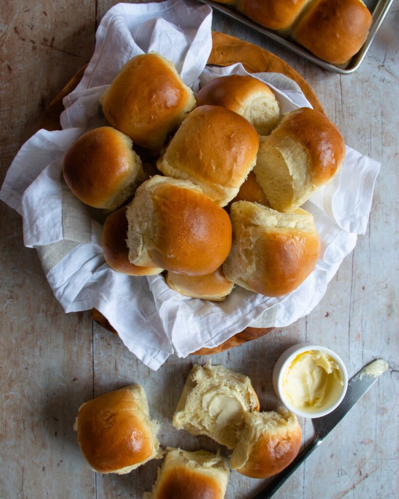 She Pan Dinner Rolls in a basket and one roll broken open and buttered.