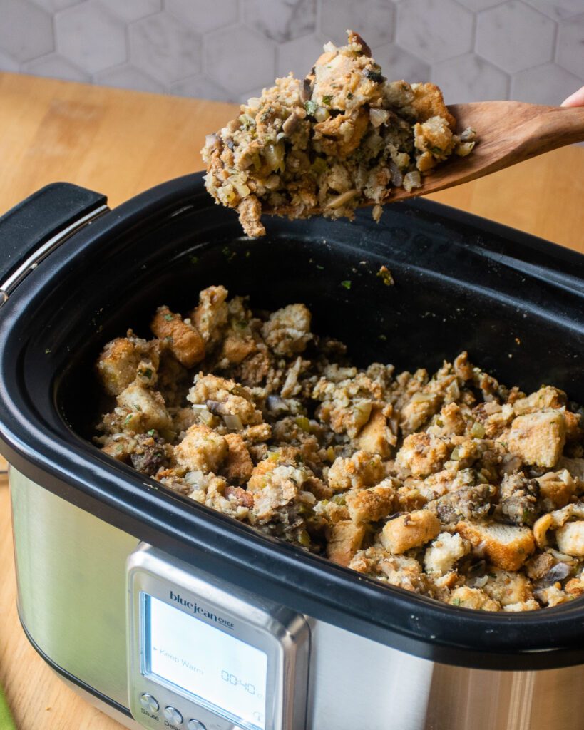 A wooden spoon scooping some Thanksgiving stuffing from a slow cooker.