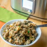 A white bowl of Thanksgiving stuffing in front of a slow cooker.