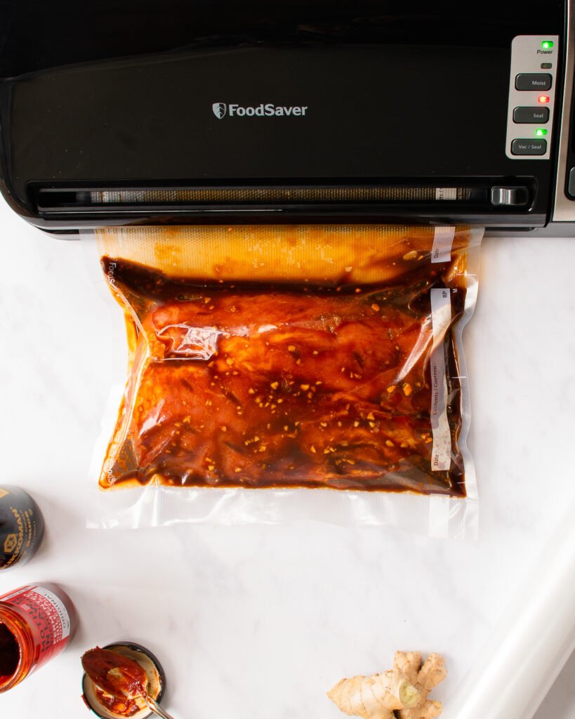Pork loin being vacuum sealed in a vacuum sealed bag with a few ingredients around.