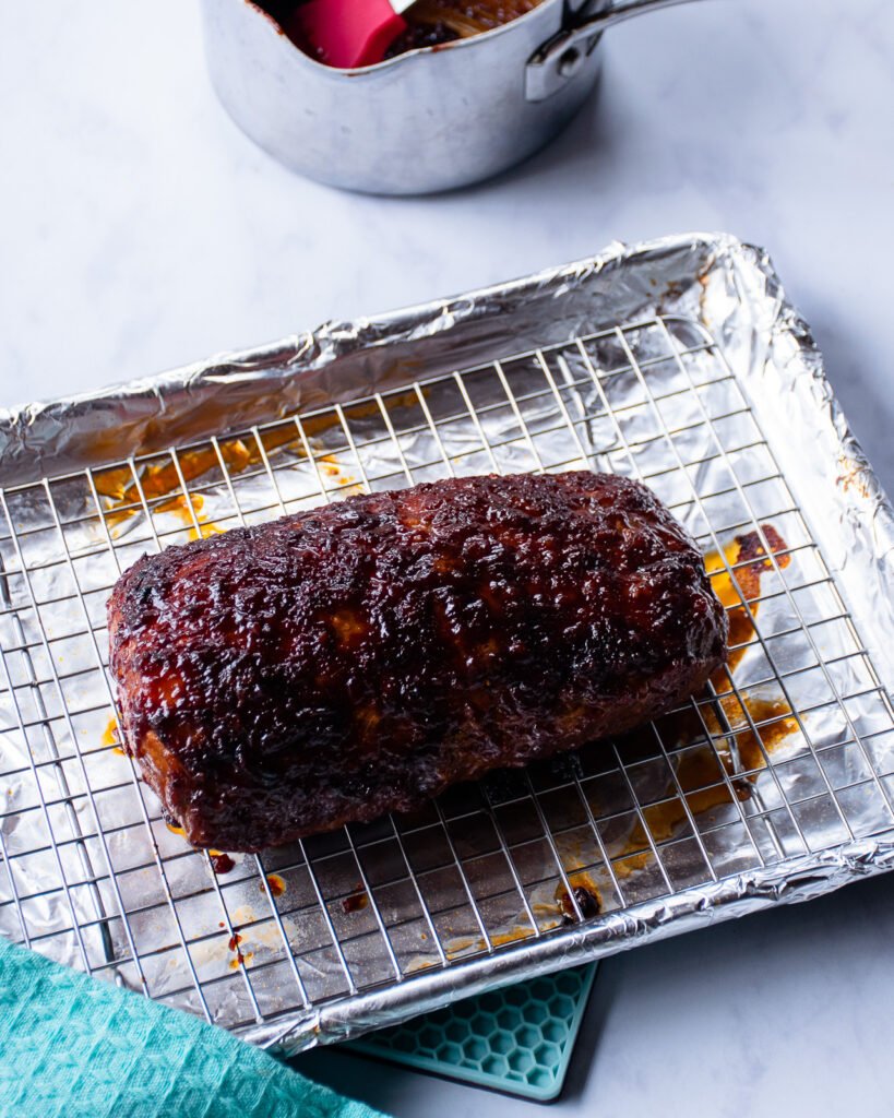 Pork Loin with BBQ sauce on a rack on a sheet pan after being broiled.