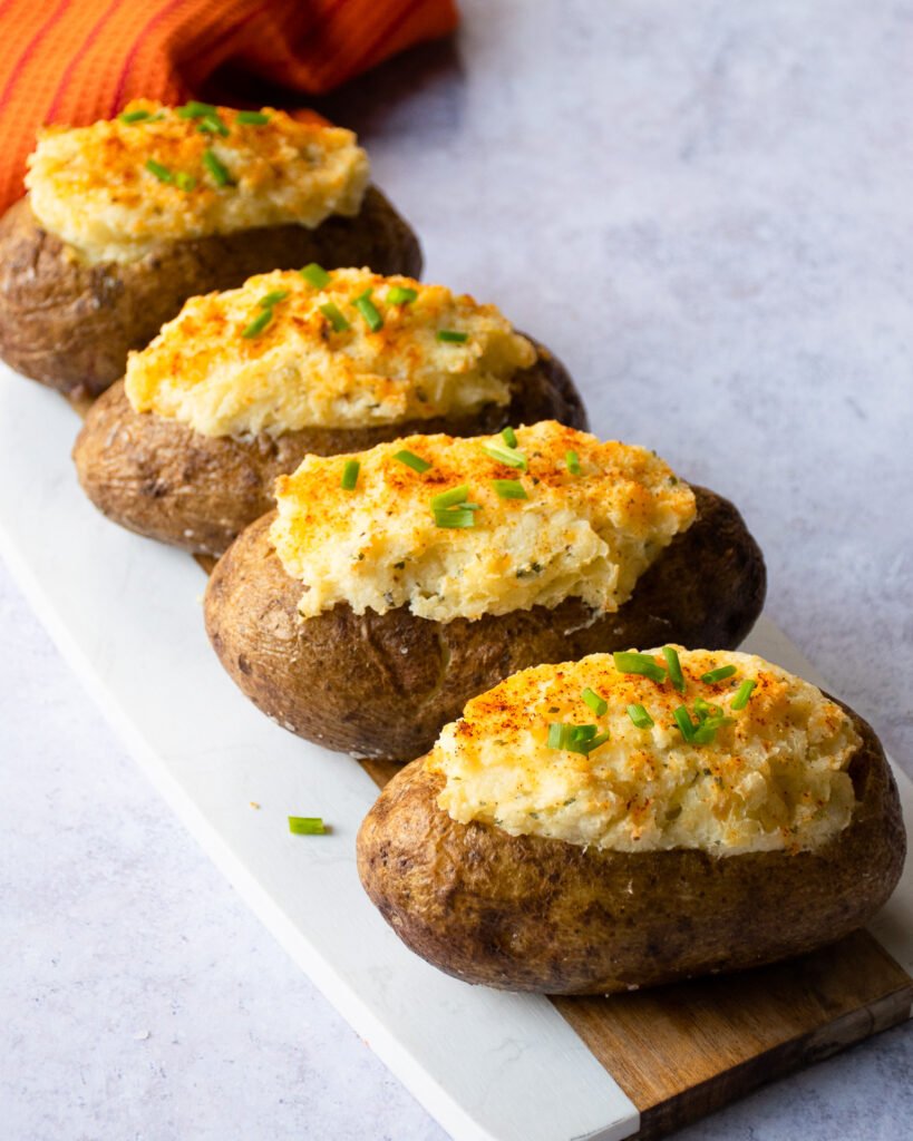 Cooked boursin twice baked stuffed potatoes on a cutting board with an orange towel in the background.