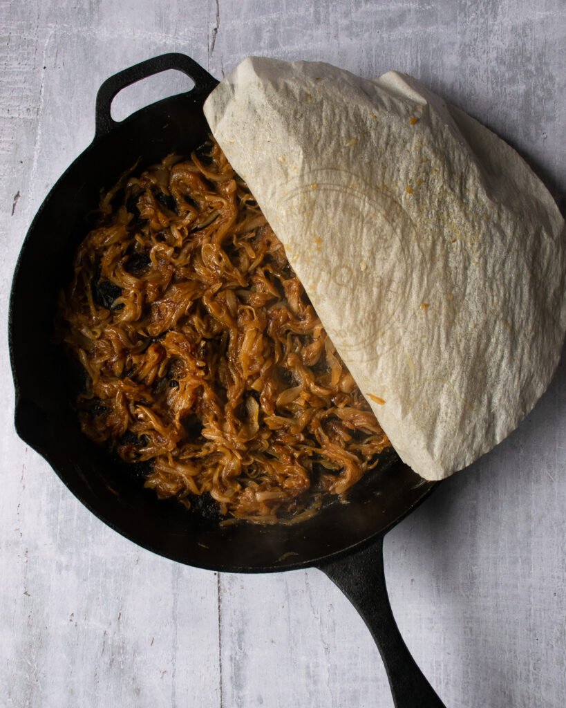 Caramelized onions in a skillet with a circle of parchment paper revealing half of the pan.
