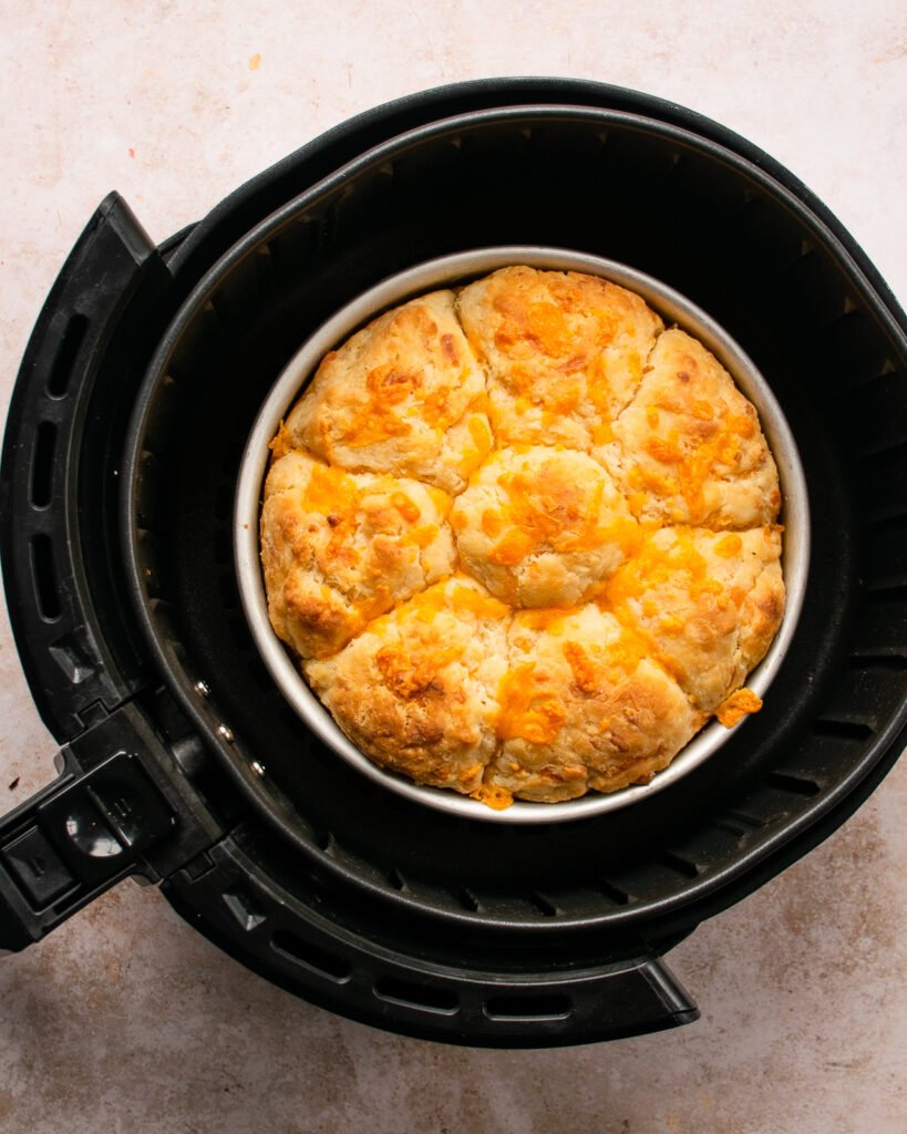 Biscuits in a cake pan in the basket of an air fryer.