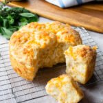 Cheddar cheese biscuits on a cooling rack with a couple broken off from the others.