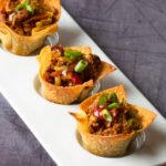 Three chicken egg roll wonton cups on a white plate.