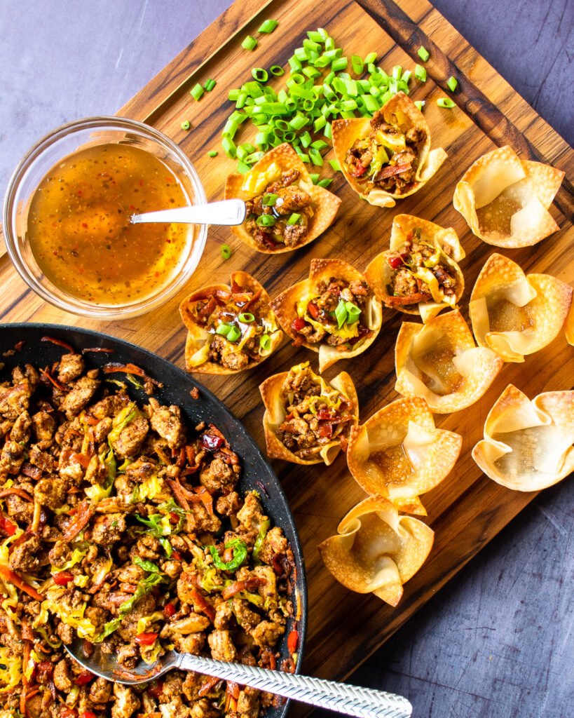 Filling chicken egg roll wonton cups with the chicken filling in aa sauce pan and the wonton cups on a cutting board.