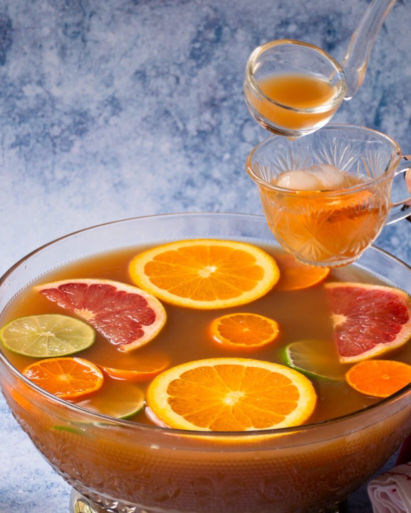 A ladle pouring tea and fruit punch into a glass tea cup.