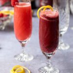 Two champagne flutes with jam bellinis on a counter.