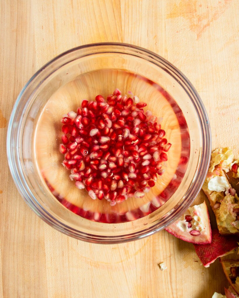 A bowl of water with pomegranate seeds in the bottom.