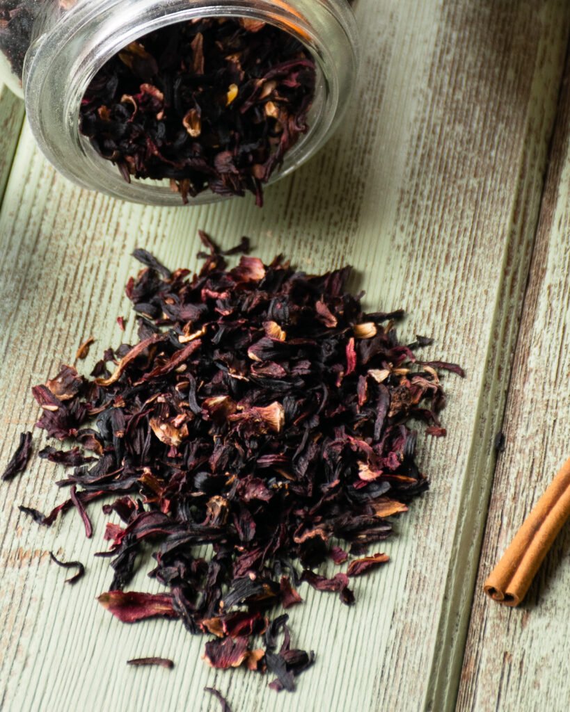 Sorrel or dried hibiscus flowers on a green wooden table with a jar behind it.