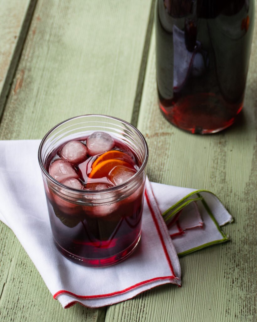 A glass of sorrel cocktail with a slice of mandarin as garnish.