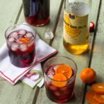Two Sorrel Cocktails in glasses with a bottle of sorrel and a bottle of rum in the background.