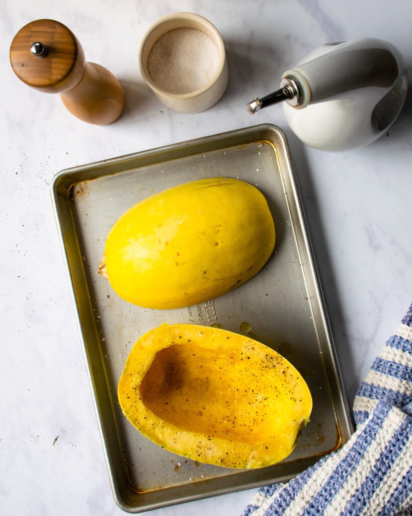 Spaghetti Squash cut in half and on a baking sheet with olive oil, salt and pepper near by.