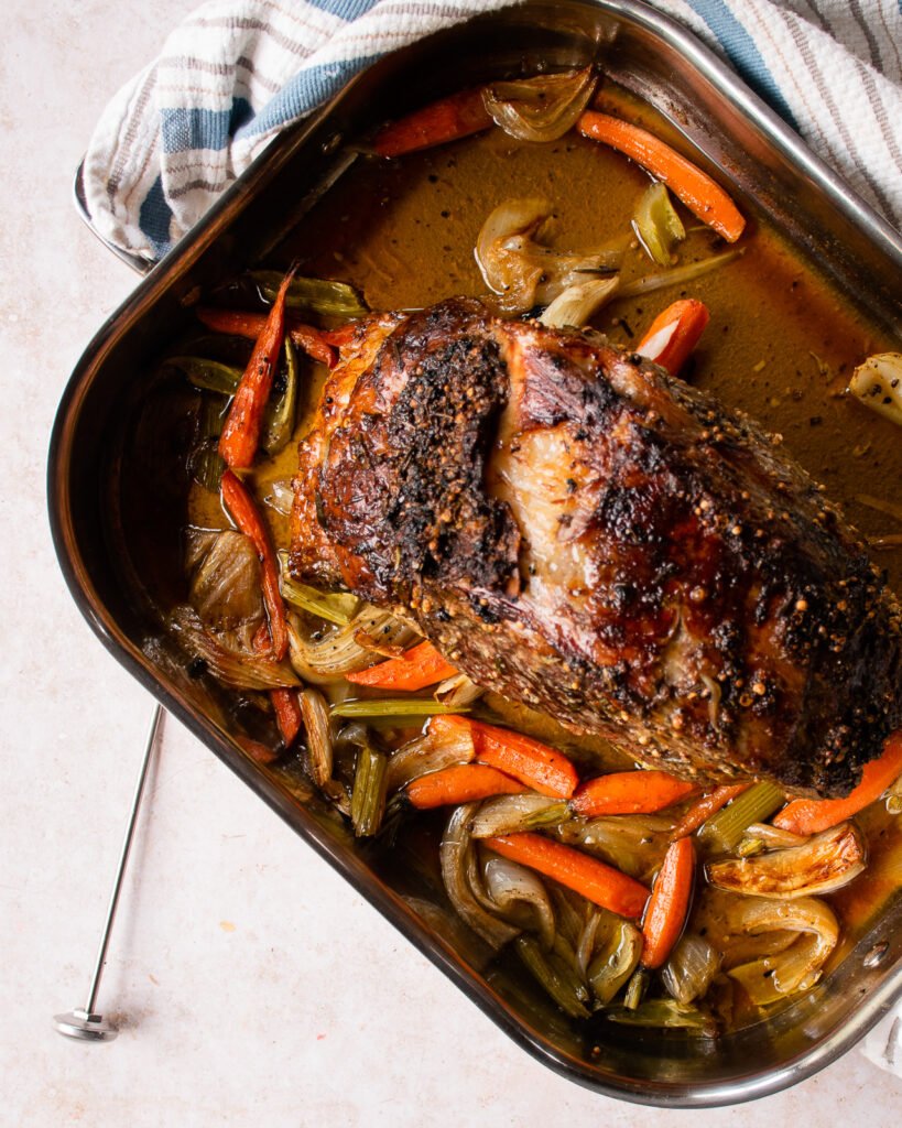 A roast beef cooked in a roasting pan with an instant read thermometer next to it.