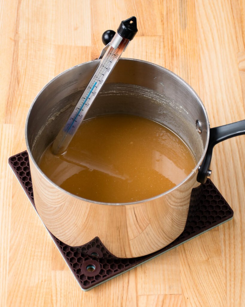 A pot of sugar and cream on a trivet with a candy thermometer sticking out of it.