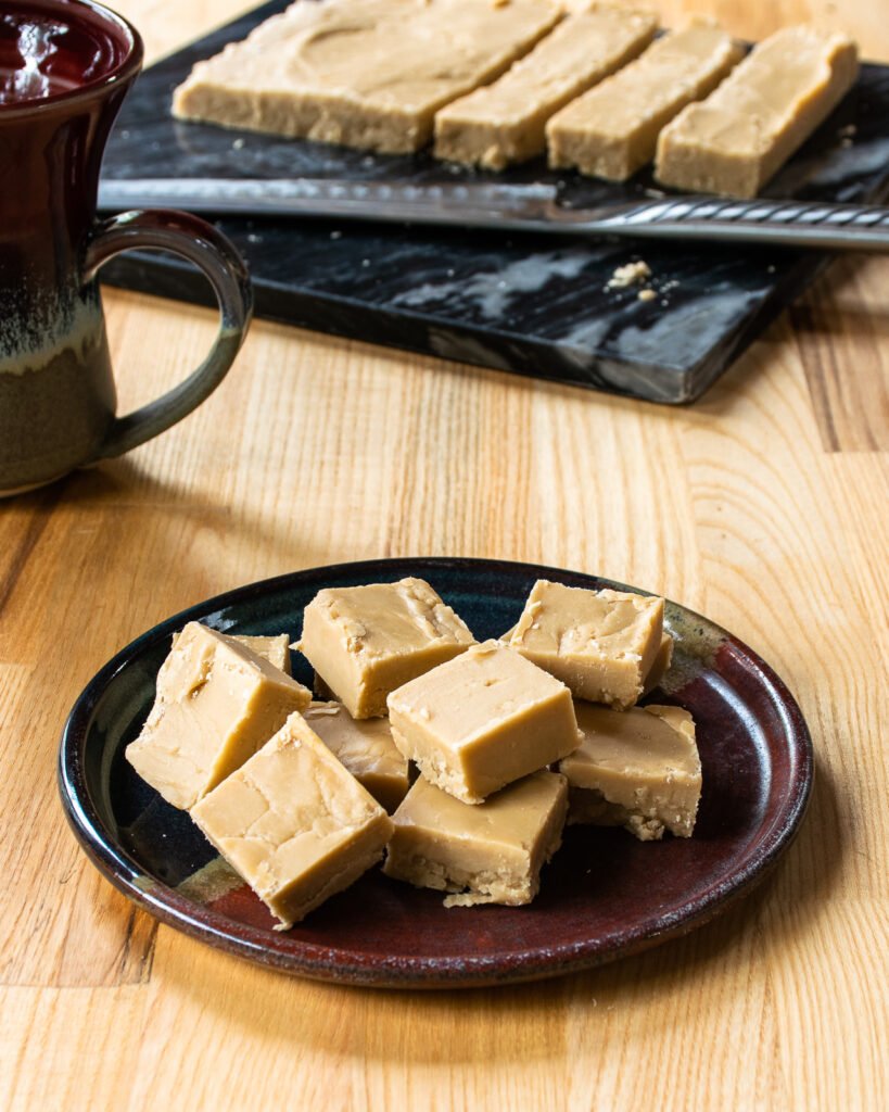 A plate of sucre à la crème squares with a mug and more fudge in background.