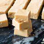 Three squares of sucre à la crème stacked on each other with more fudge in the background.