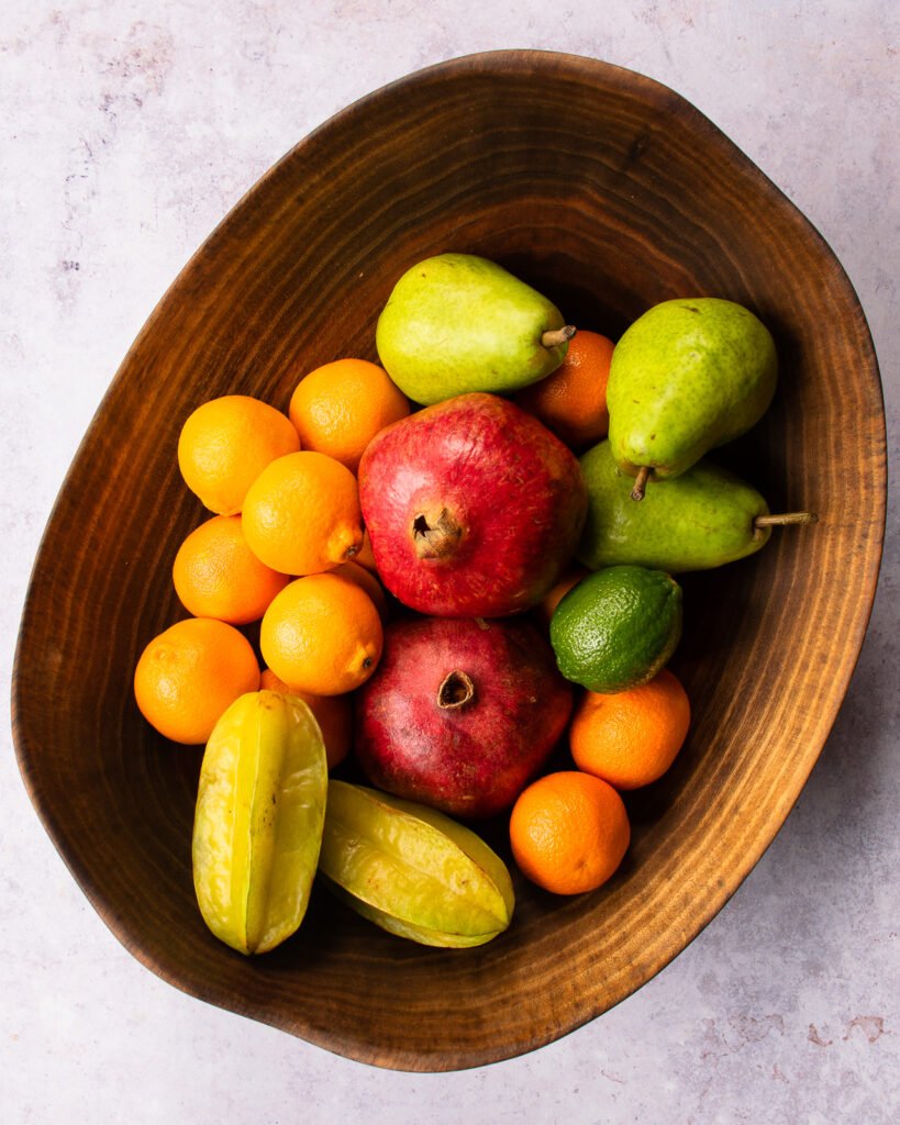 A wooden bowl of fruit including starfruit, mandarins, pears and pomegranate.