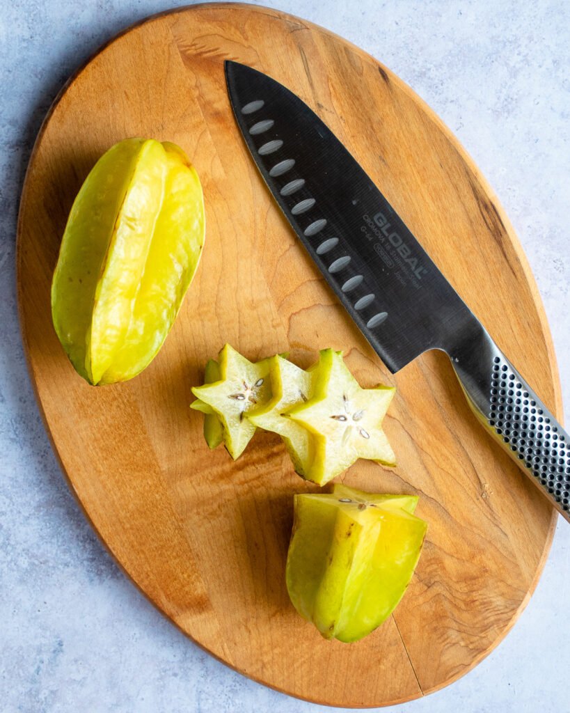 A starfruit being cut on a wooden cutting board with a knife.
