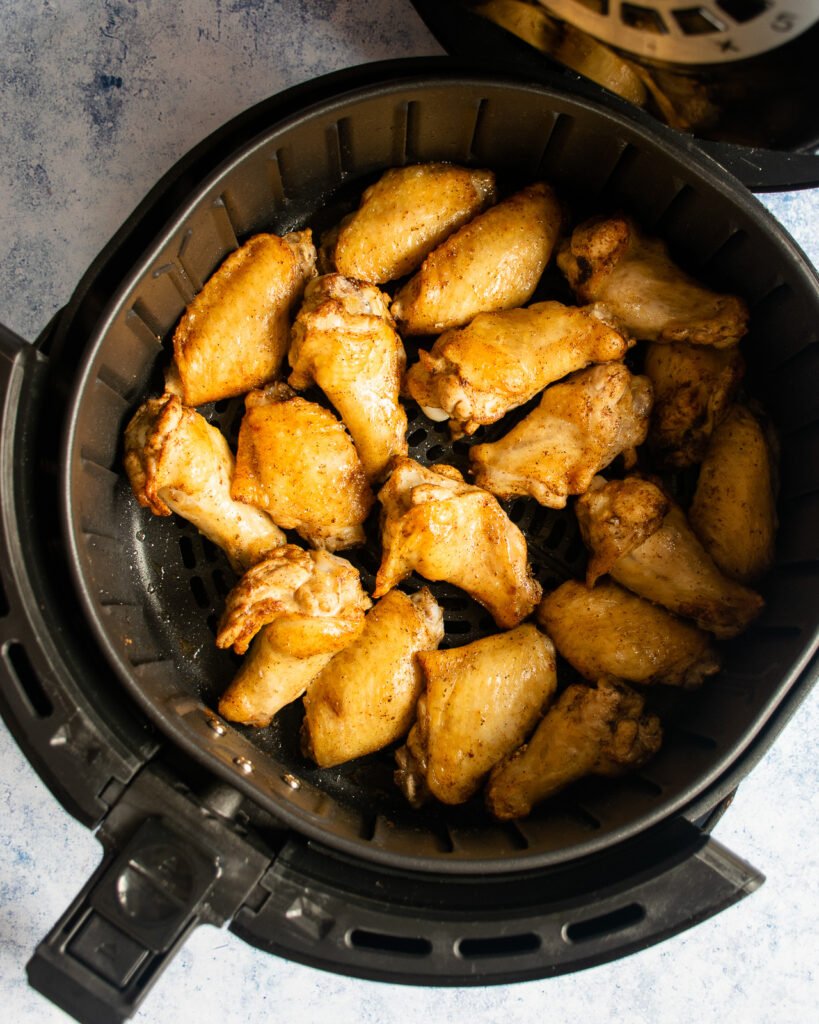 Chicken wings partially cooked in an air fryer basket.