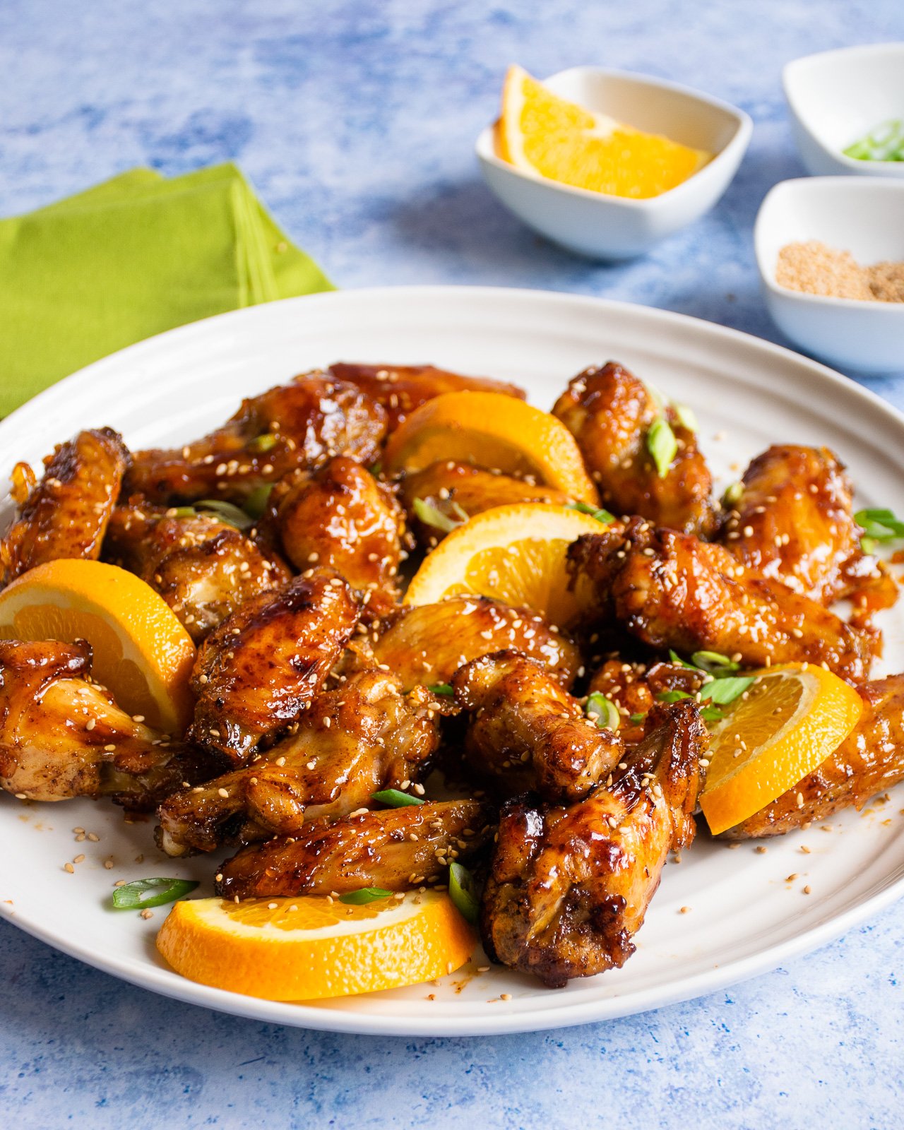 Air Fryer Orange Sesame Chicken Wings on a white platter with sesame seeds, orange slices and sliced scallions on a white platter on a blue marble countertop.