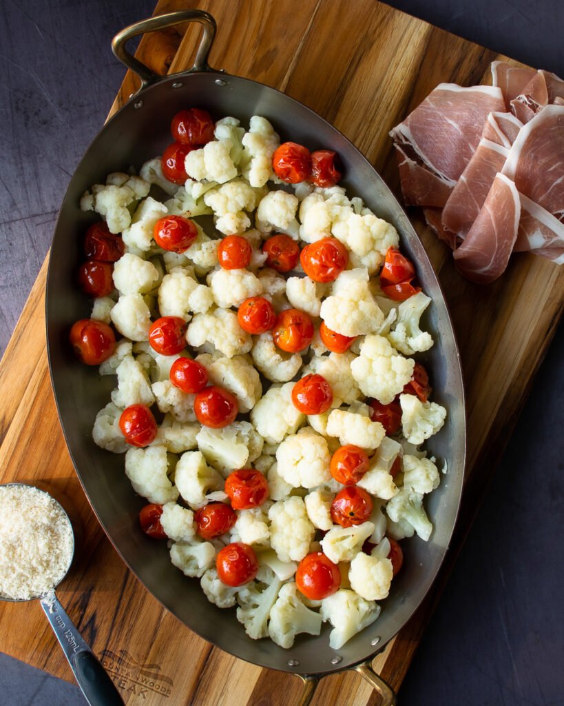 Gratin pan with cauliflower and tomatoes, prosciutto on the side and cheese on the side.