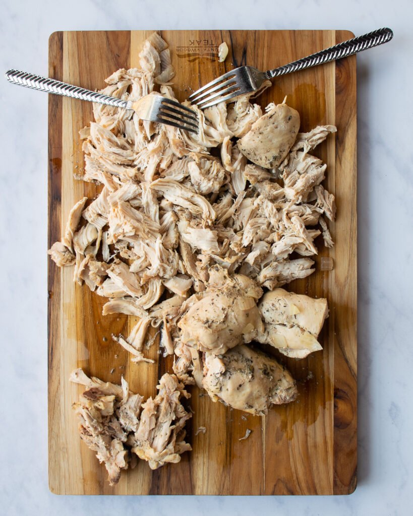 Shredded chicken on a wooden board with two forks.