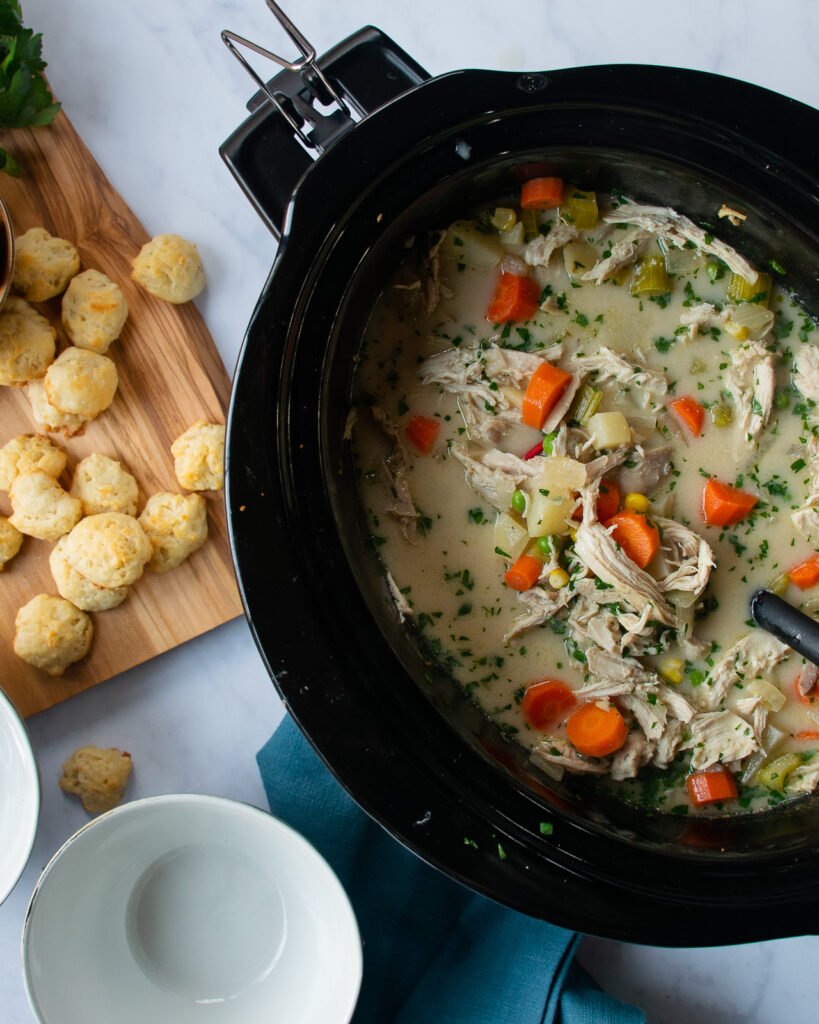 A slow cooker with soup in it and biscuit croutons on the side.