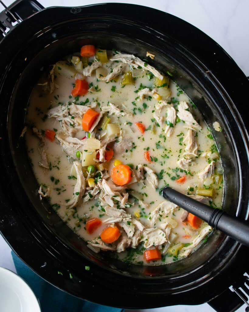 Chicken pot pie soup in a slow cooker with a laadle sticking out.
