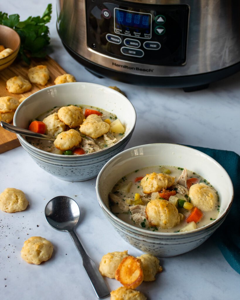 Two bowls of slow cooker chicken pot pie soup in front of a slow cooker