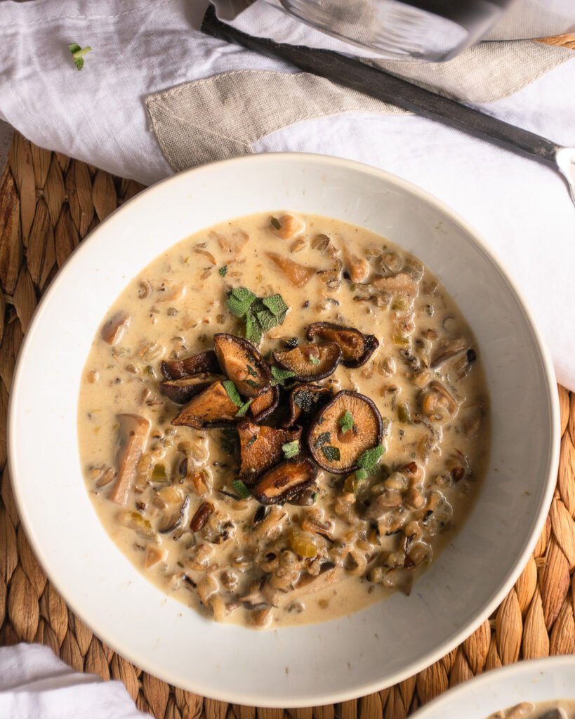 A bowl of cream of mushroom soup on a rattan mat with napkin and spoon.