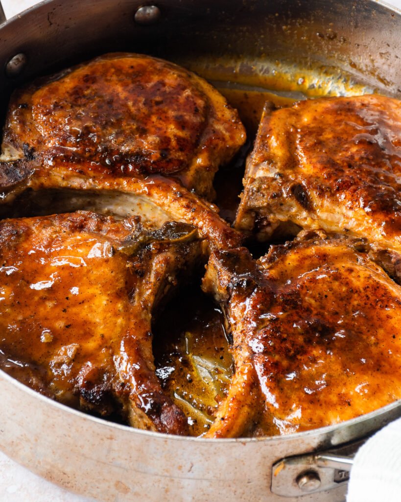 Four pork chops turned over and glazed in a saute pan.
